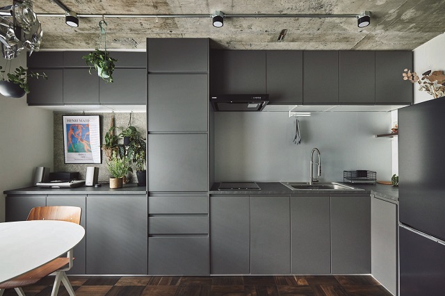 マットなグレーで統一されたキッチンは、 IKEAのシステムを利用。取っ手のないシンプルなデザインが美しい。換気扇のダクトは、吊り戸棚に合わせてつくった扉で隠している
