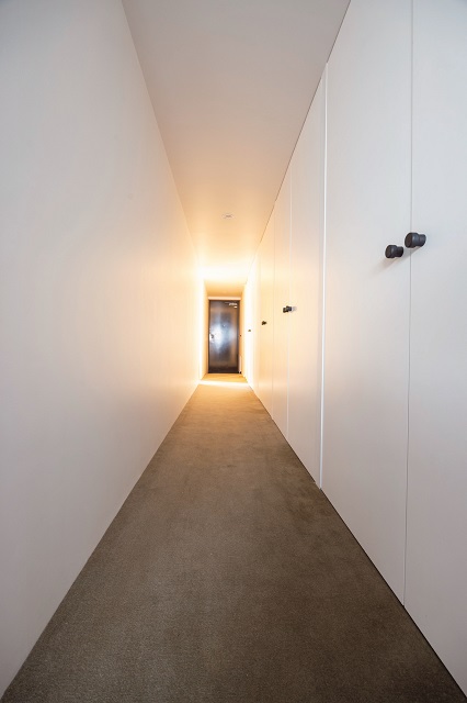 カーペット敷きの長い廊下がM邸の個性に。右側に並ぶ建具はトイレのドア以外は造作したもの。枠のないフラットな収まりにこだわった